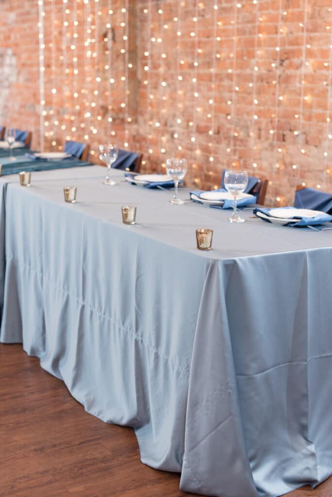 head table with slate blue linens in front of exposed brick wall